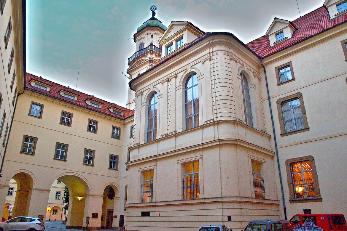 A cream-coloured wing of the Klementinum with tall arched windows around a courtyard, and the Astronomical Tower behind it