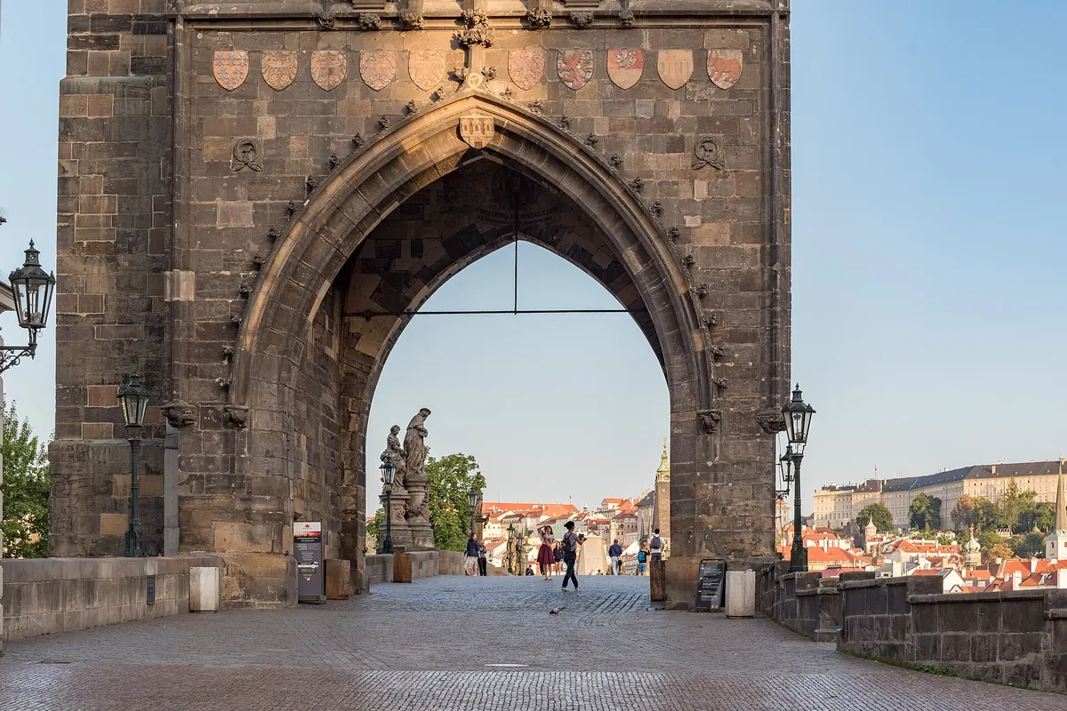 The pointed Gothic arch of the Old Town Bridge Tower, framing the start of Charles Bridge and a lamp-lit street