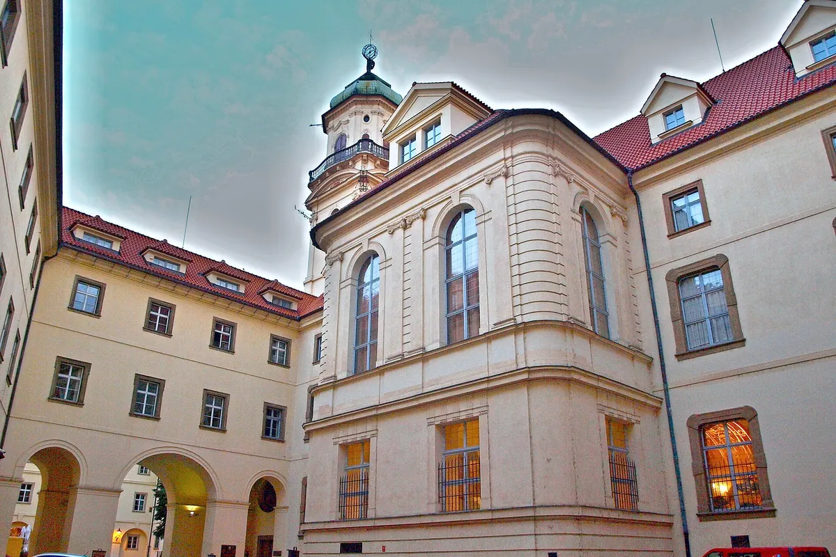 A cream-coloured wing of the Klementinum with tall arched windows around a courtyard, and the Astronomical Tower rising behind it