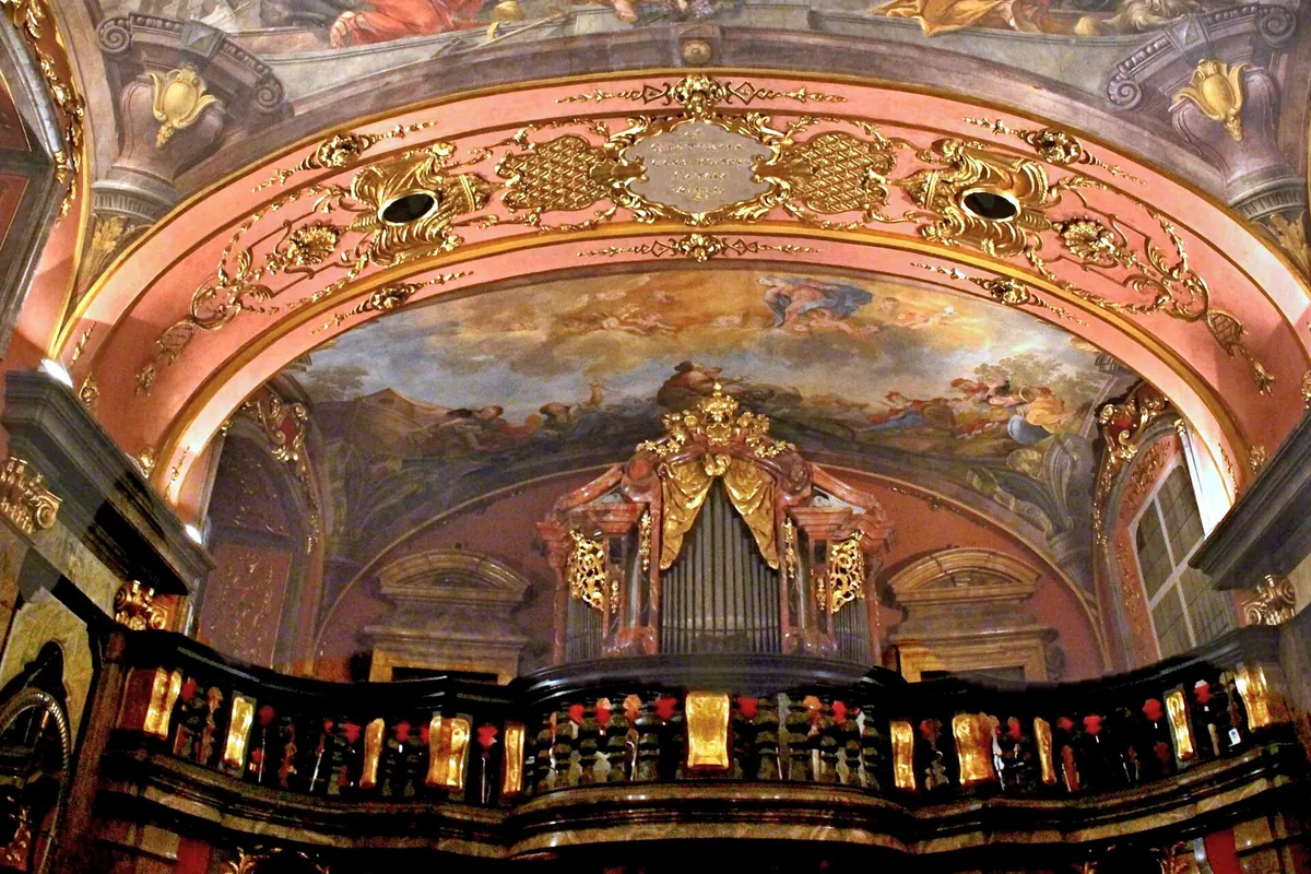 The choir loft of the Mirror Chapel with its black and gold balustrade, a Baroque organ and the painted ceiling above